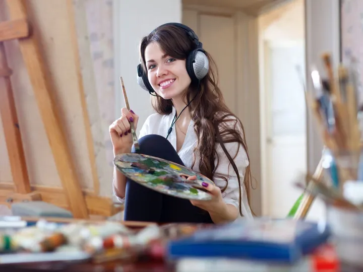 Long-haired woman in headphones  paints with oil colors