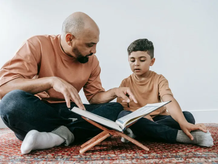 A father guides his son in reading a book, promoting learning and bonding.