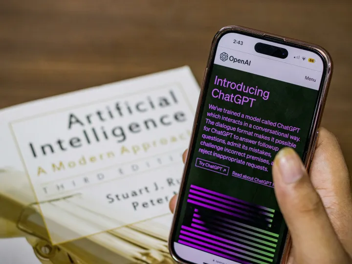Close-up of a smartphone displaying ChatGPT app held over AI textbook.