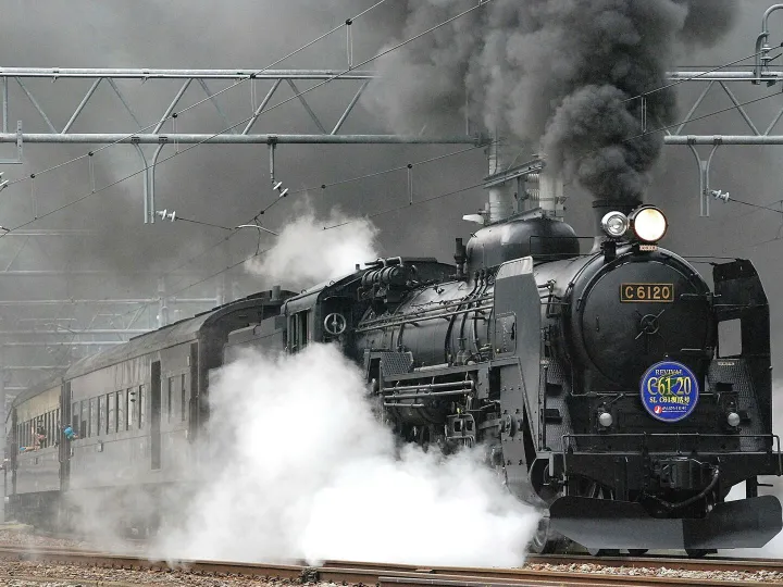 Steam locomotive releasing smoke and steam on a rail track, showcasing vintage train transportation.