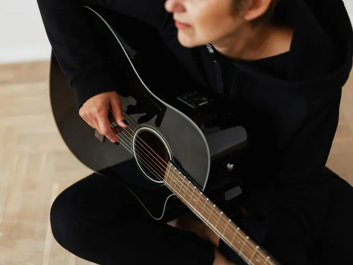 Person playing an acoustic guitar indoors, focusin