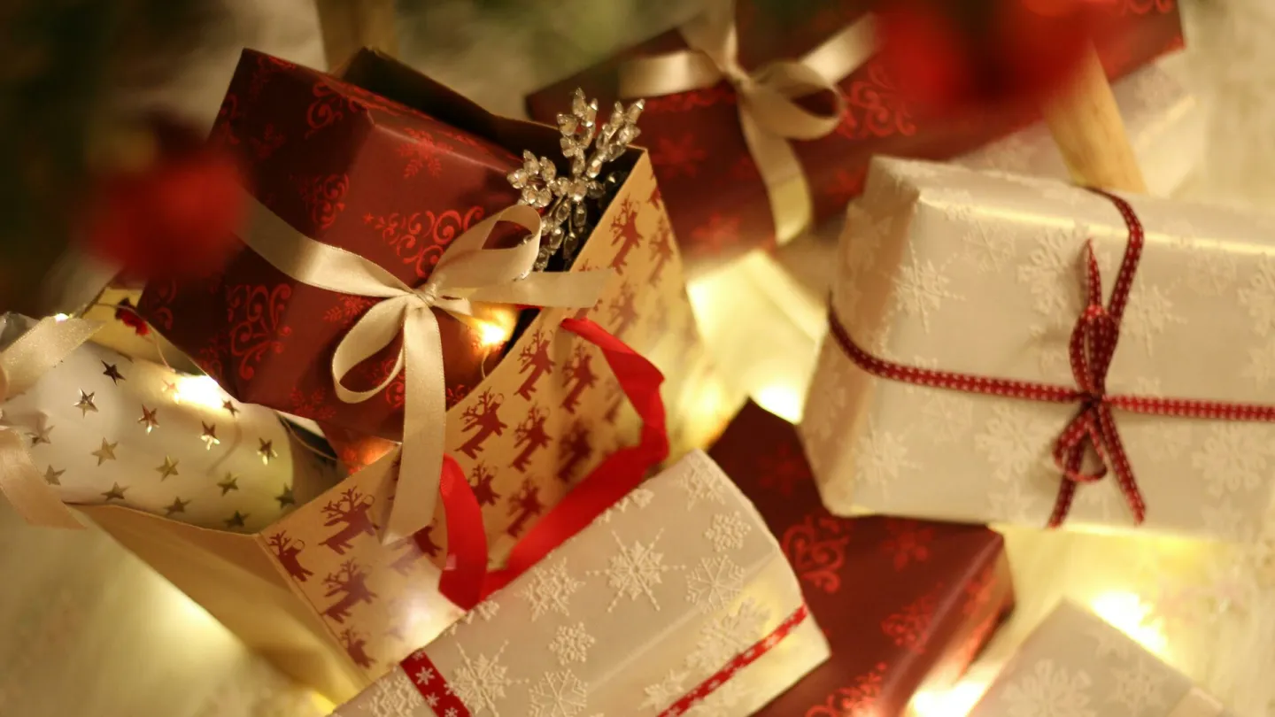 Beautifully wrapped Christmas presents under the tree with festive decorations and ribbons.